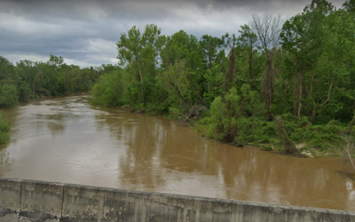 A muddy river flows through a lush green landscape under a cloudy sky.