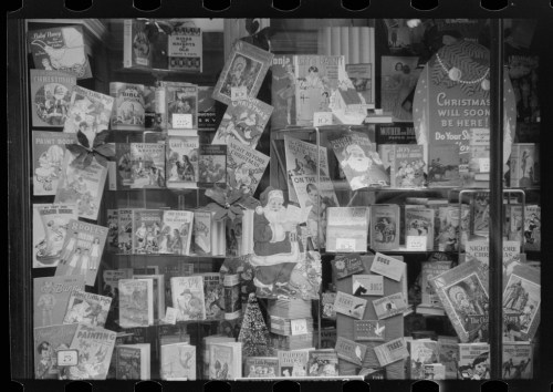 A vintage storefront display filled with colorful holiday-themed books and decorations, featuring Santa Claus.