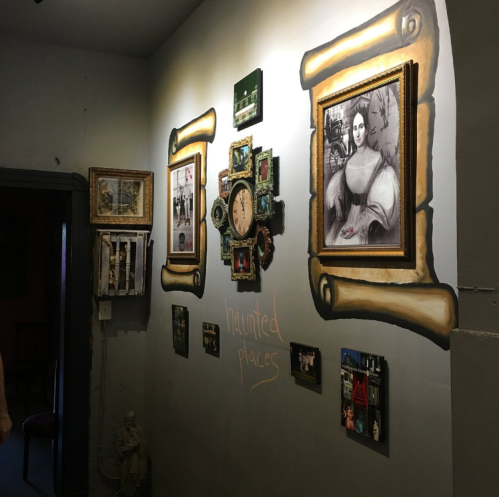A wall decorated with framed photos and artwork, featuring the words "haunted places" in chalk.
