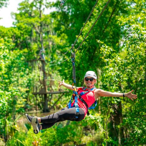 A person in athletic wear zip-lining through a lush green forest, smiling and enjoying the adventure.