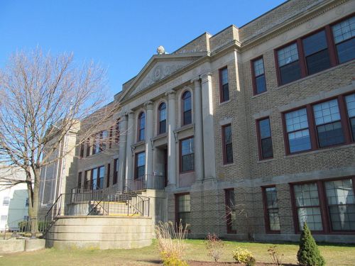 Historic brick building with large entrance steps, tall windows, and a clear blue sky in the background.