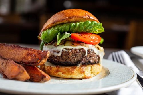 A juicy burger with lettuce, tomato, and cheese, served with crispy potato wedges on a plate.