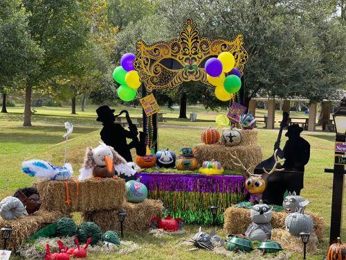A festive display with decorated pumpkins, hay bales, and colorful balloons, featuring silhouettes of musicians in a park.