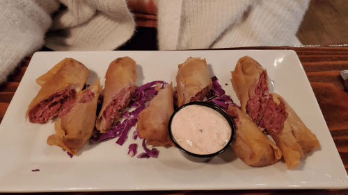 A plate of crispy spring rolls filled with meat, served with a dipping sauce and garnished with purple cabbage.