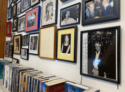 A wall covered with framed photos and artwork, alongside a shelf of books.