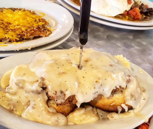 A plate of biscuits and gravy topped with a knife, with a side of cheesy hash browns in the background.