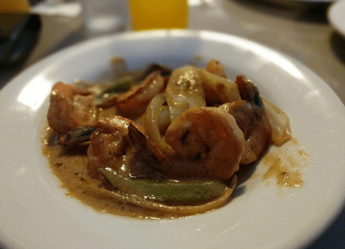 A plate of shrimp cooked in a creamy sauce with vegetables, including onions and green peppers.
