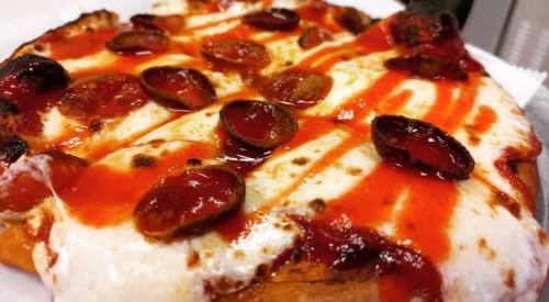 A close-up of a pepperoni pizza with melted cheese and drizzled tomato sauce on top.