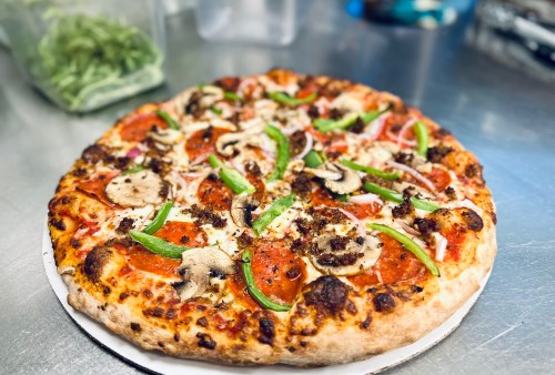 A freshly baked pizza topped with pepperoni, mushrooms, green peppers, onions, and cheese on a wooden board.