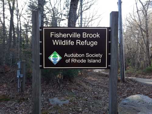 Sign for Fisherville Brook Wildlife Refuge, managed by the Audubon Society of Rhode Island, surrounded by trees.