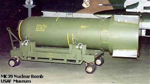 Image of an MK-39 nuclear bomb displayed on a wheeled cart at the USAF Museum, featuring a green cylindrical body.