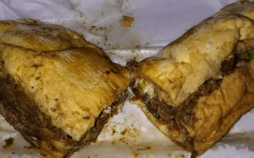 A close-up of a split sandwich filled with shredded beef, vegetables, and a golden-brown bread exterior.