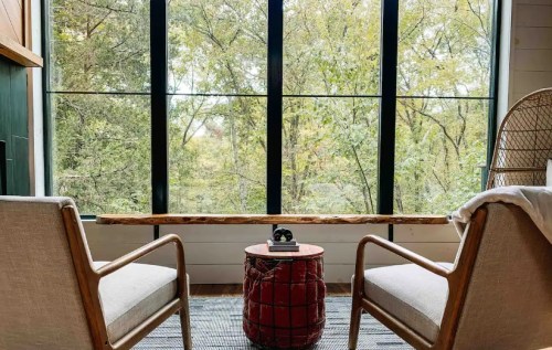 Cozy seating area with two chairs and a round table, framed by large windows overlooking a lush, green landscape.