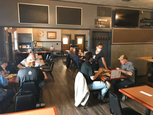 A casual restaurant interior with diners at tables, a server delivering food, and a relaxed atmosphere.