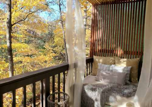 Cozy outdoor seating area with cushions, surrounded by vibrant autumn foliage and soft drapes.