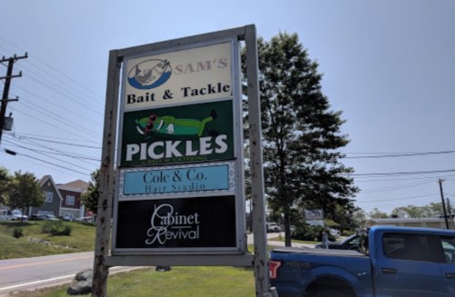 Sign for Sam's Bait & Tackle, featuring a pickle mascot, with listings for nearby businesses including a hair studio.
