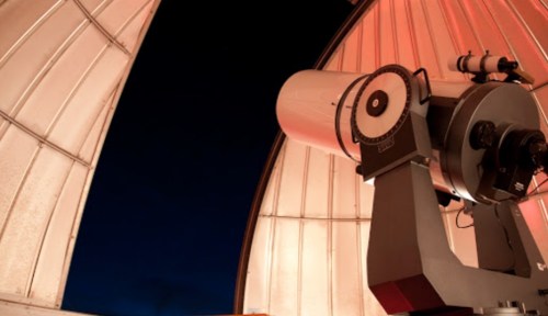 A telescope inside an observatory dome, with a dark night sky visible outside.