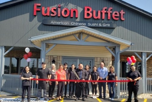 A group of people stands outside Fusion Buffet, holding a ribbon for a grand opening, with balloons in the background.