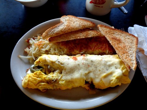 A plate of a fluffy omelet with cheese, hash browns, and two slices of toasted bread.