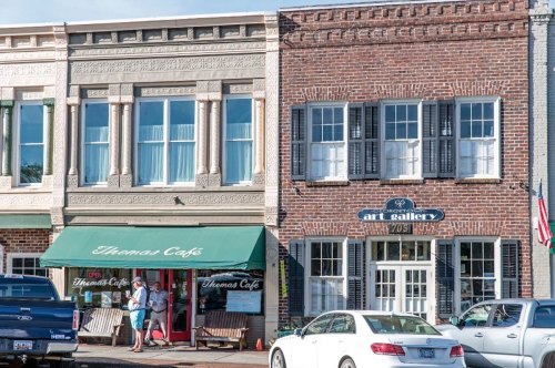 A charming street scene featuring Thomas Café and an art gallery with brick facades and outdoor seating.