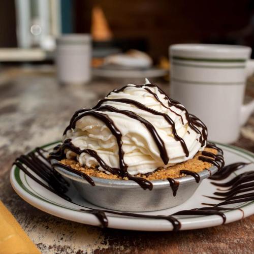 A small pie topped with whipped cream and chocolate drizzle, served on a plate with a rustic wooden table in the background.