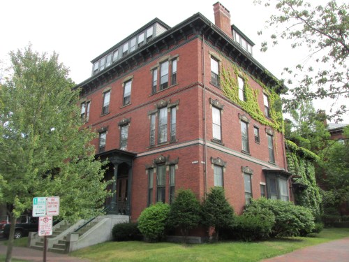 A large red brick building with ivy climbing its walls, surrounded by trees and greenery.