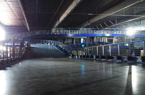 An empty indoor space with a sloped ramp and a blue railing, illuminated by bright lights from above.