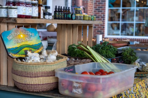 A vibrant market display featuring fresh vegetables, herbs, and jars of preserves on a wooden table.