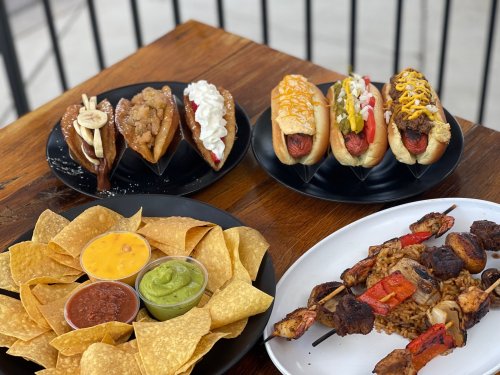A table with plates of hot dogs, dessert waffles, chips with dips, and skewers over rice.
