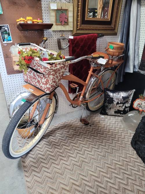 A vintage-style bicycle with a decorative basket, set against a backdrop of eclectic decor and a patterned rug.