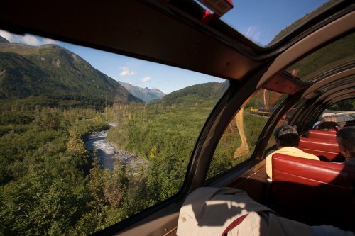 View from a train window showcasing a lush green valley and a winding river surrounded by mountains.