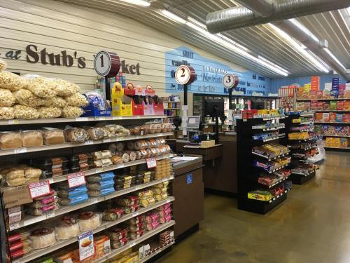 Interior of a grocery store with shelves of snacks, baked goods, and a checkout counter in the background.
