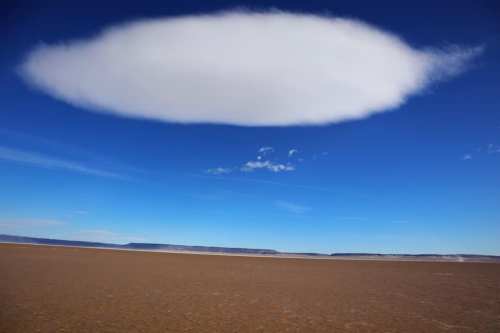A vast, barren landscape under a blue sky with a large, oval cloud hovering above.