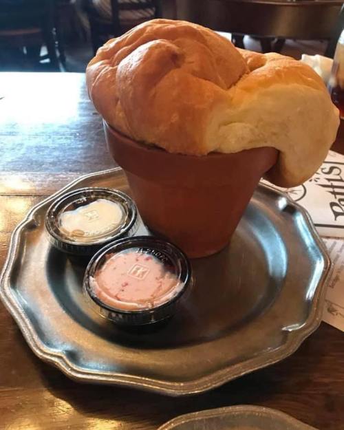A fluffy bread roll shaped like a flower pot, served with two small containers of dipping sauces on a metal plate.