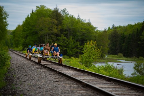 A group of people riding a rail bike along a scenic railway track surrounded by lush greenery and a calm lake.