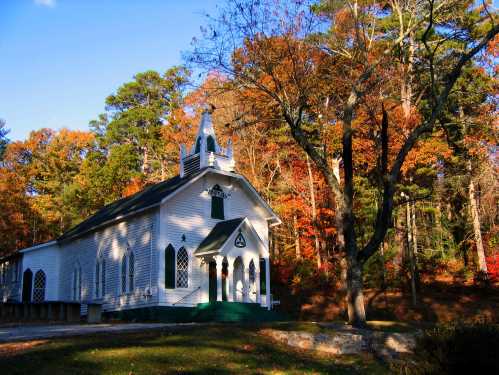 A quaint white church surrounded by colorful autumn trees under a clear blue sky.