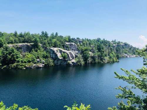 Scenic view of a calm lake surrounded by rocky cliffs and lush greenery under a clear blue sky.