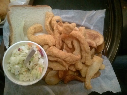 A plate of crispy fried fish, served with a side of coleslaw and slices of white bread.