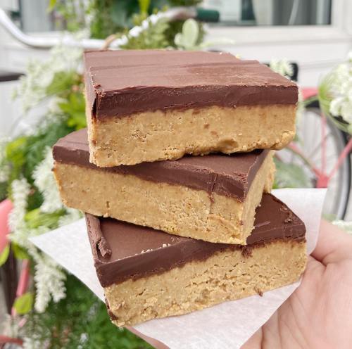 Three layers of chocolate and peanut butter bars stacked on a white napkin, with greenery in the background.