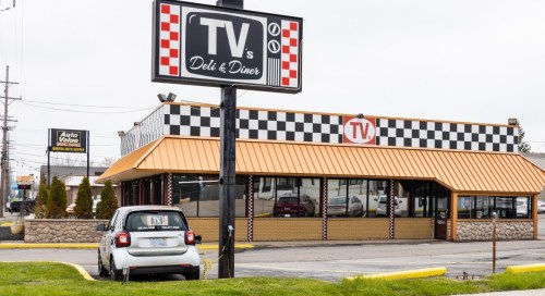 A diner with a checkered exterior and a sign reading "TV's Deli & Diner," featuring a small car parked outside.