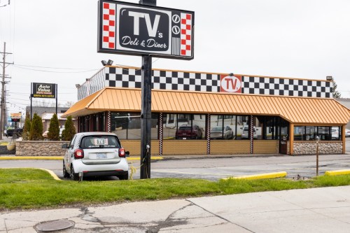A diner with a checkered exterior and a sign reading "TV's Deli & Diner," parked car in front.
