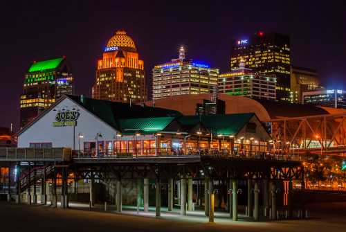 Night view of a waterfront restaurant with city skyline illuminated in the background.