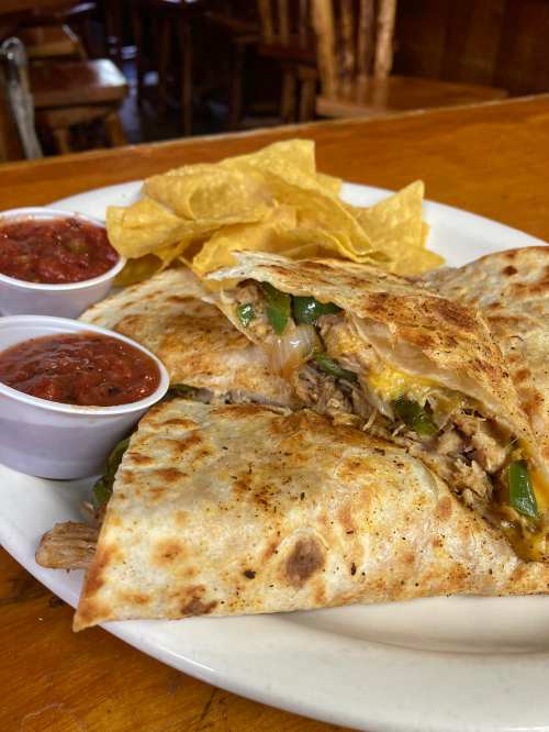 A plate featuring a grilled quesadilla filled with chicken and peppers, served with tortilla chips and two cups of salsa.