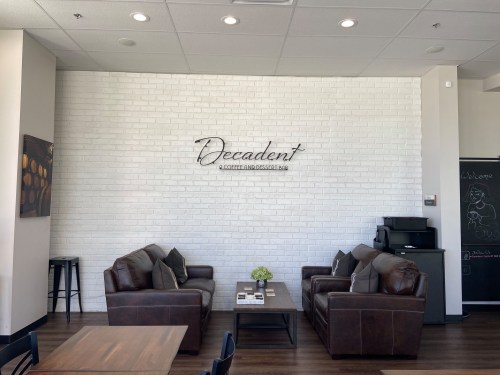 Cozy café interior with leather sofas, a white brick wall, and a sign reading "Decadent Coffee and Dessert."