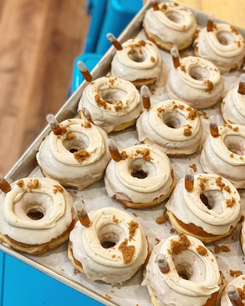 A tray of frosted donuts topped with crumbs and filled with syringes, showcasing a creative dessert presentation.