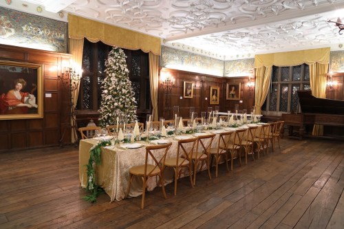 A beautifully set dining table in an elegant room, featuring a Christmas tree and ornate decor.