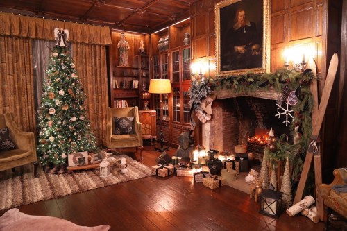 Cozy holiday living room with a decorated Christmas tree, fireplace, and festive decor, featuring warm lighting and wooden accents.