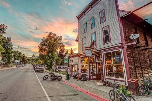 A quaint street scene featuring a vintage building, parked vehicles, and bicycles, with a colorful sunset in the background.