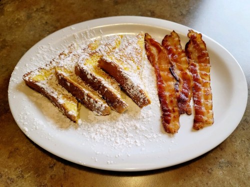 A plate of French toast dusted with powdered sugar, accompanied by crispy bacon strips.