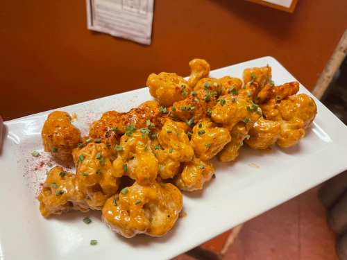 A white plate holds crispy cauliflower bites drizzled with a creamy sauce and sprinkled with green onions.